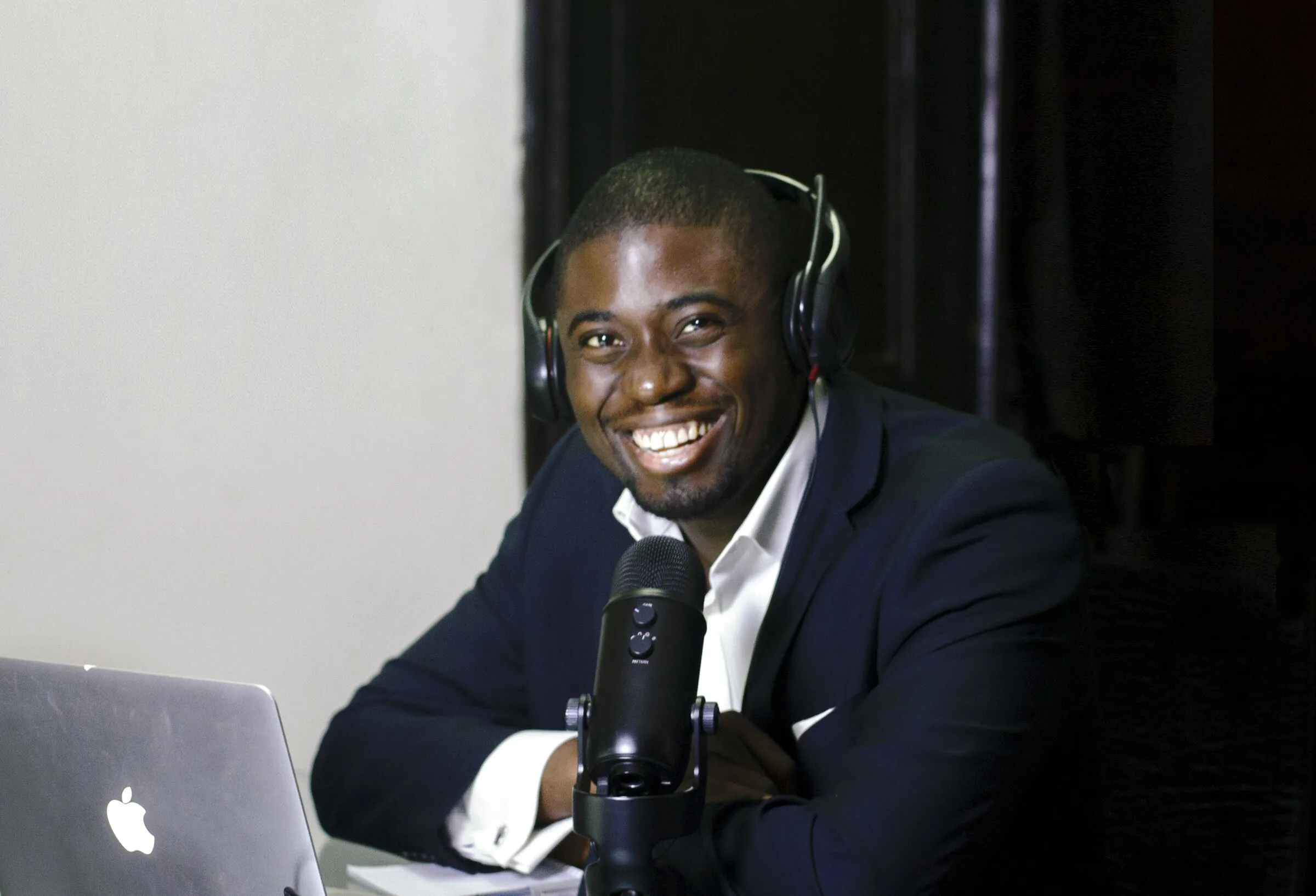 Chi Odogwu laughing mid-interview, headphones on, at a podcast microphone
