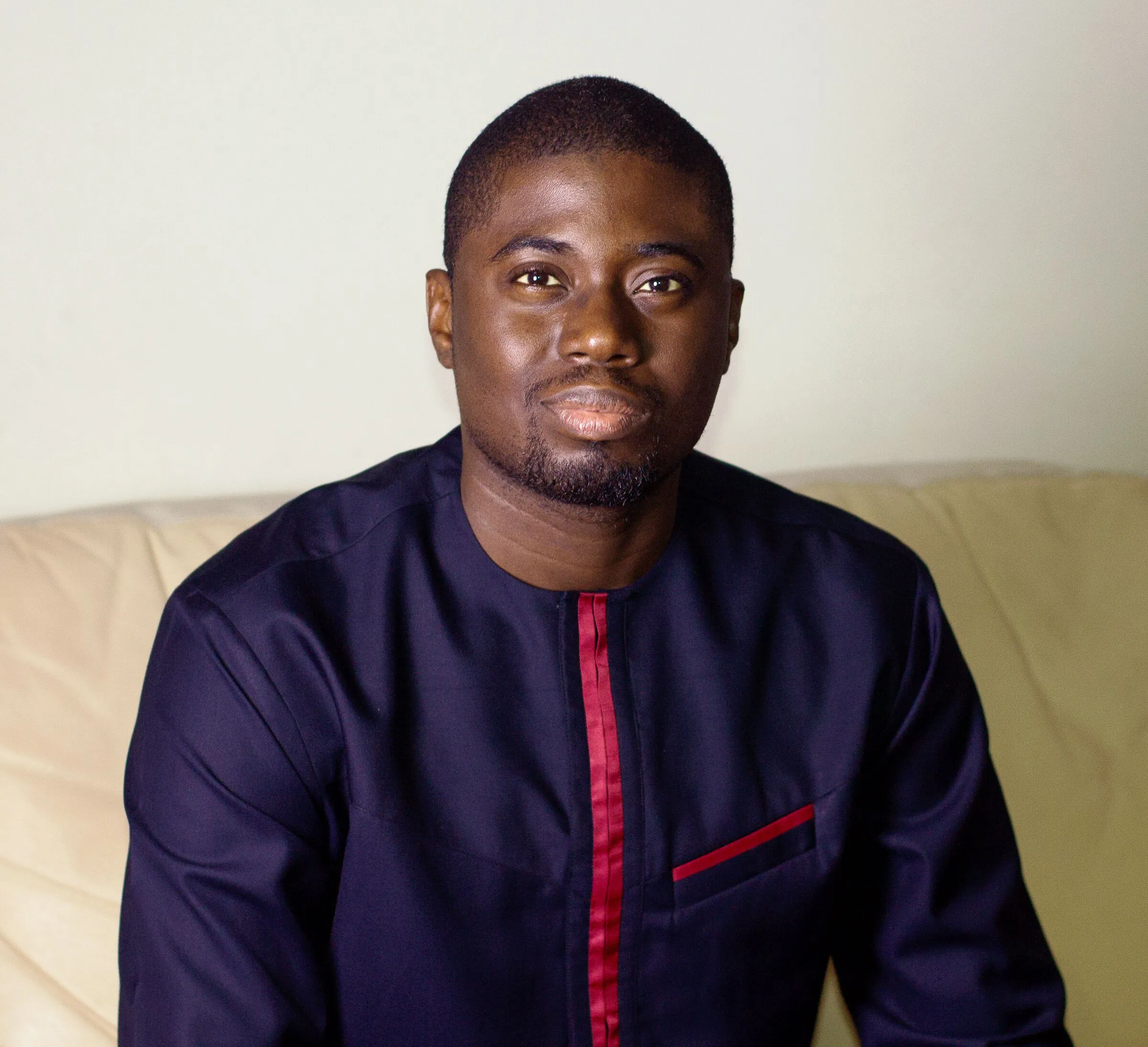 Chi Odogwu in a navy kaftan with red trim, seated