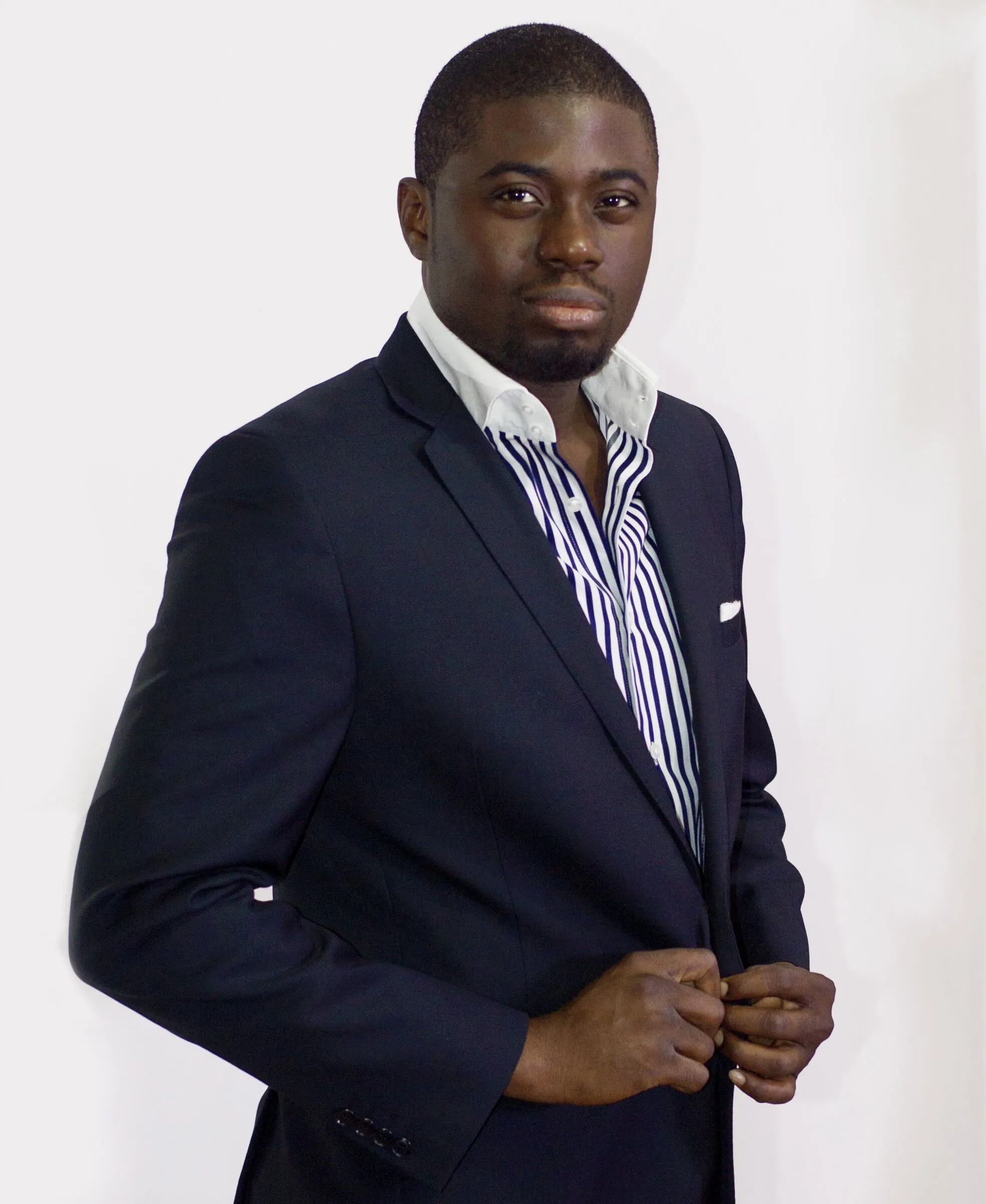 Chi Odogwu standing, buttoning a navy suit jacket